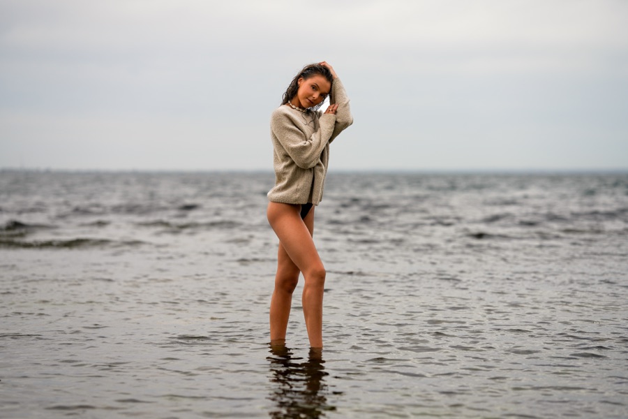 Model in an oversized knit standing in shallow water under overcast light