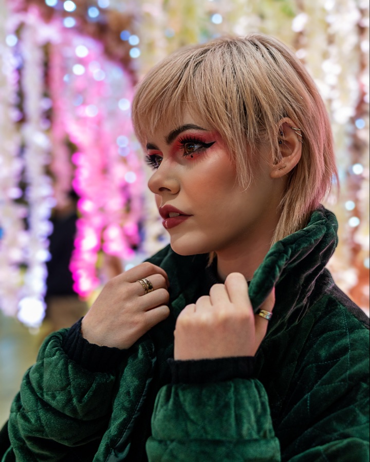 Editorial portrait in a green velvet jacket against strung lights