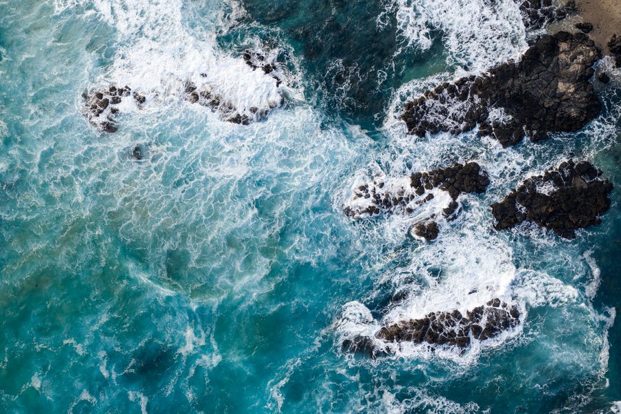 Top down aerial of whitewater breaking over dark coastal rock