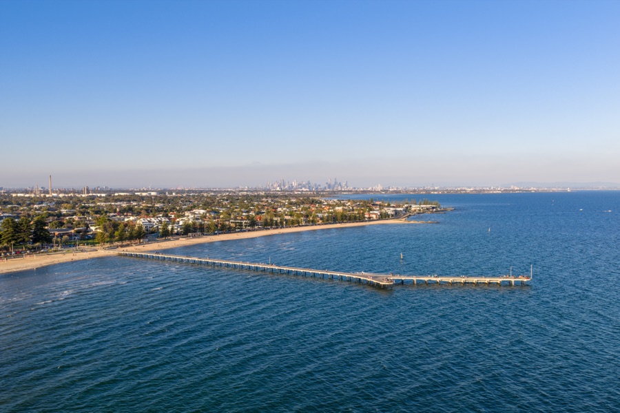 Aerial view along a Port Phillip Bay pier with the Melbourne CBD skyline on the horizon