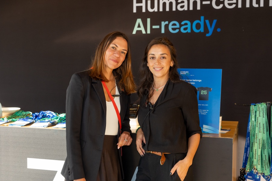 Two delegates photographed at the registration desk of an AI event