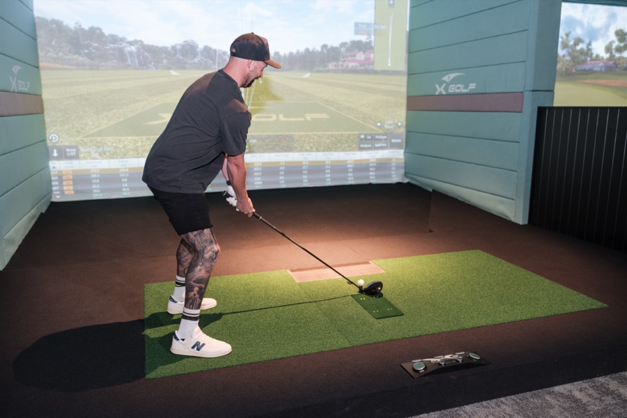 Player mid swing in an indoor golf simulator bay