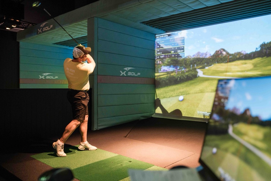 Golfer mid swing in a simulator bay at XGOLF