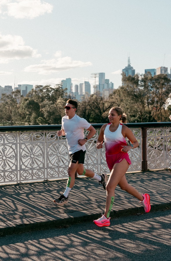 Two runners crossing a bridge with the city behind
