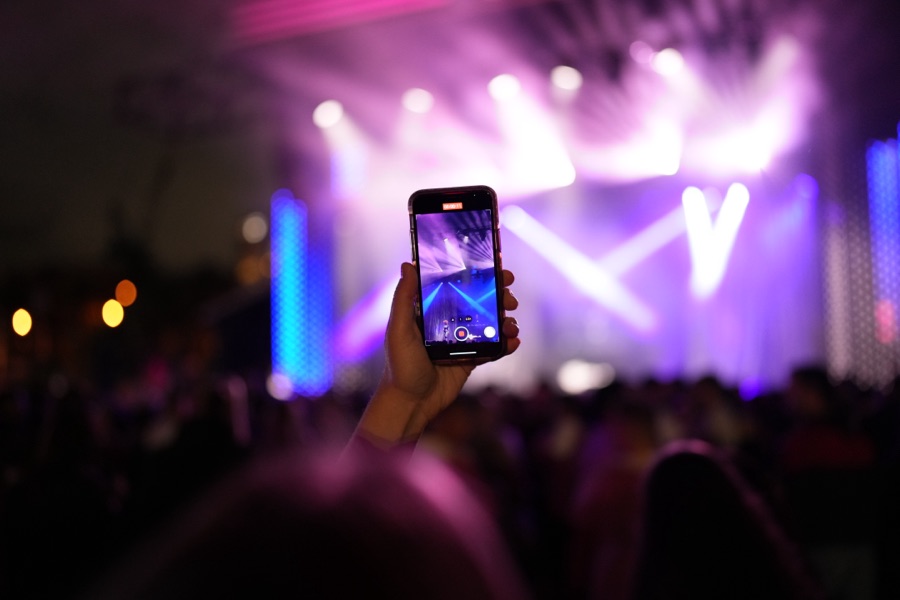 Phone raised in a crowd under purple stage light