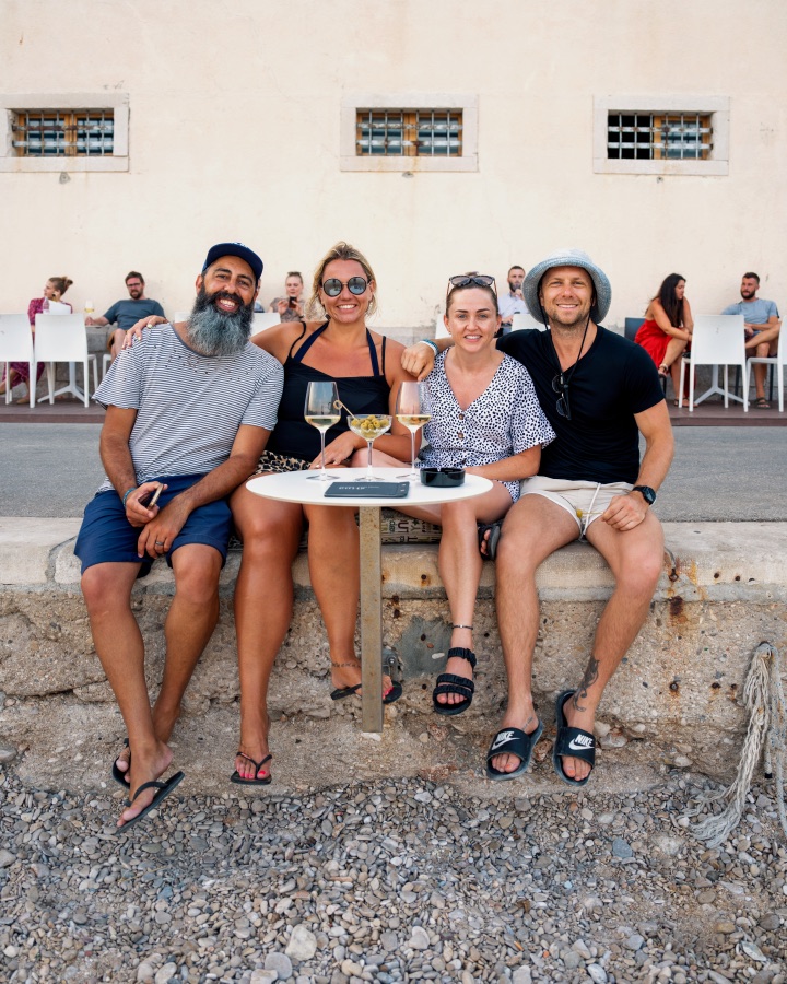 Four friends with drinks at a table against a stone wall