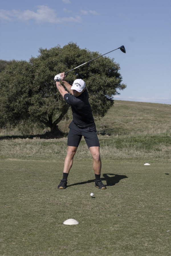 Golfer mid swing on a fairway lined with gums