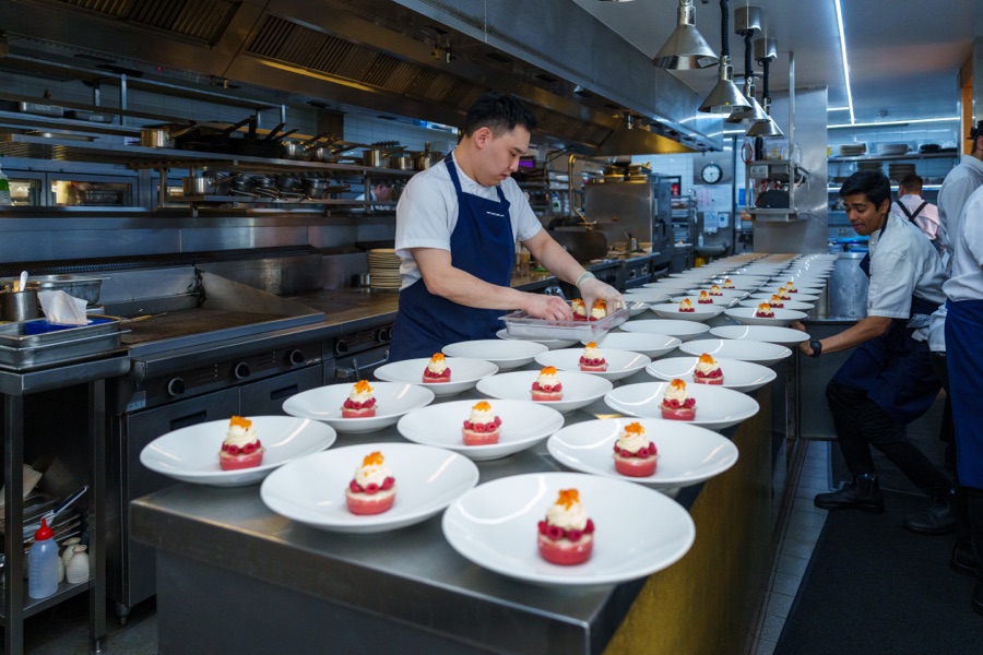 Chefs plating desserts along a commercial kitchen pass