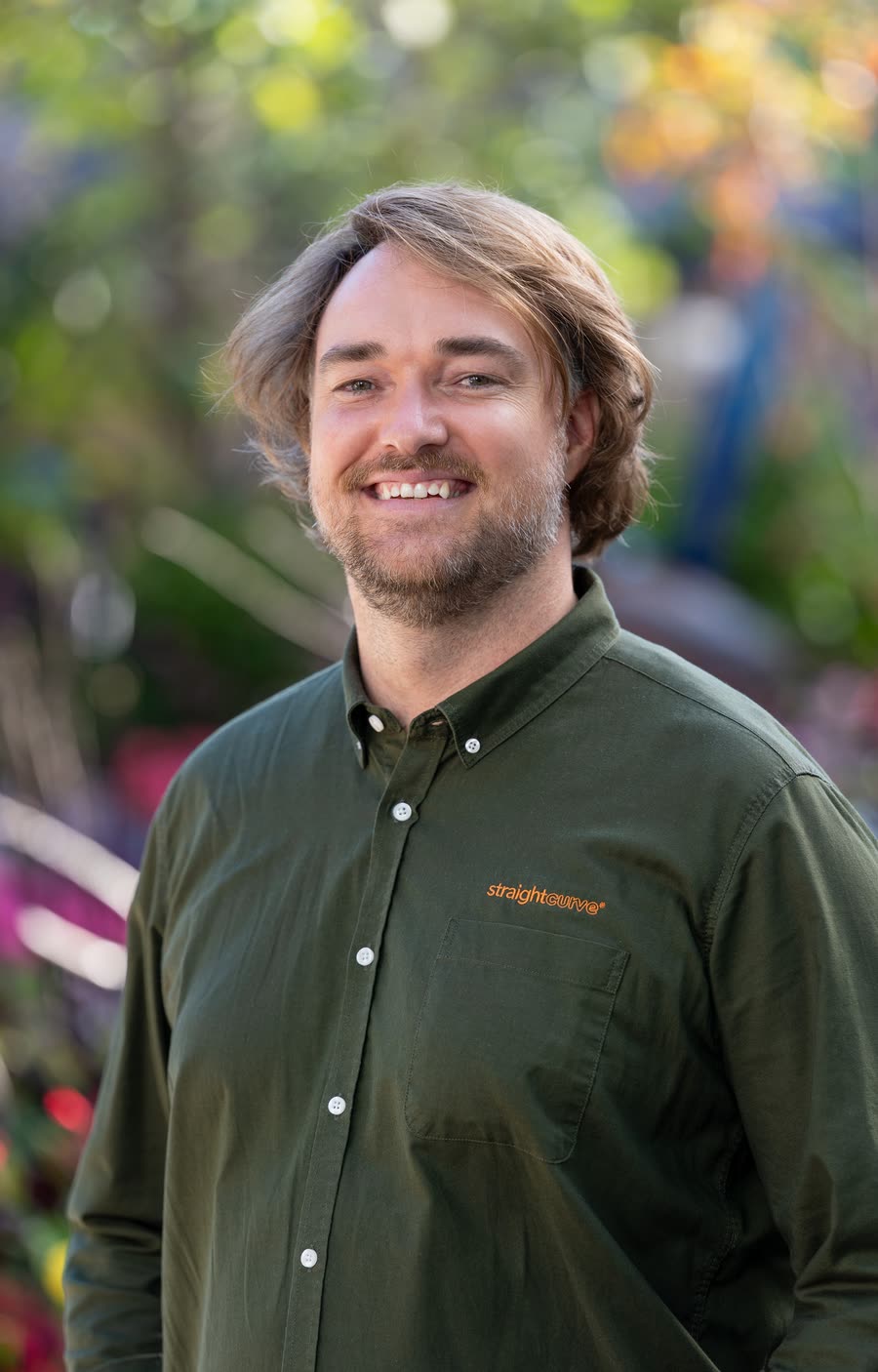 Corporate headshot of a team member in a branded green shirt among garden nursery planting