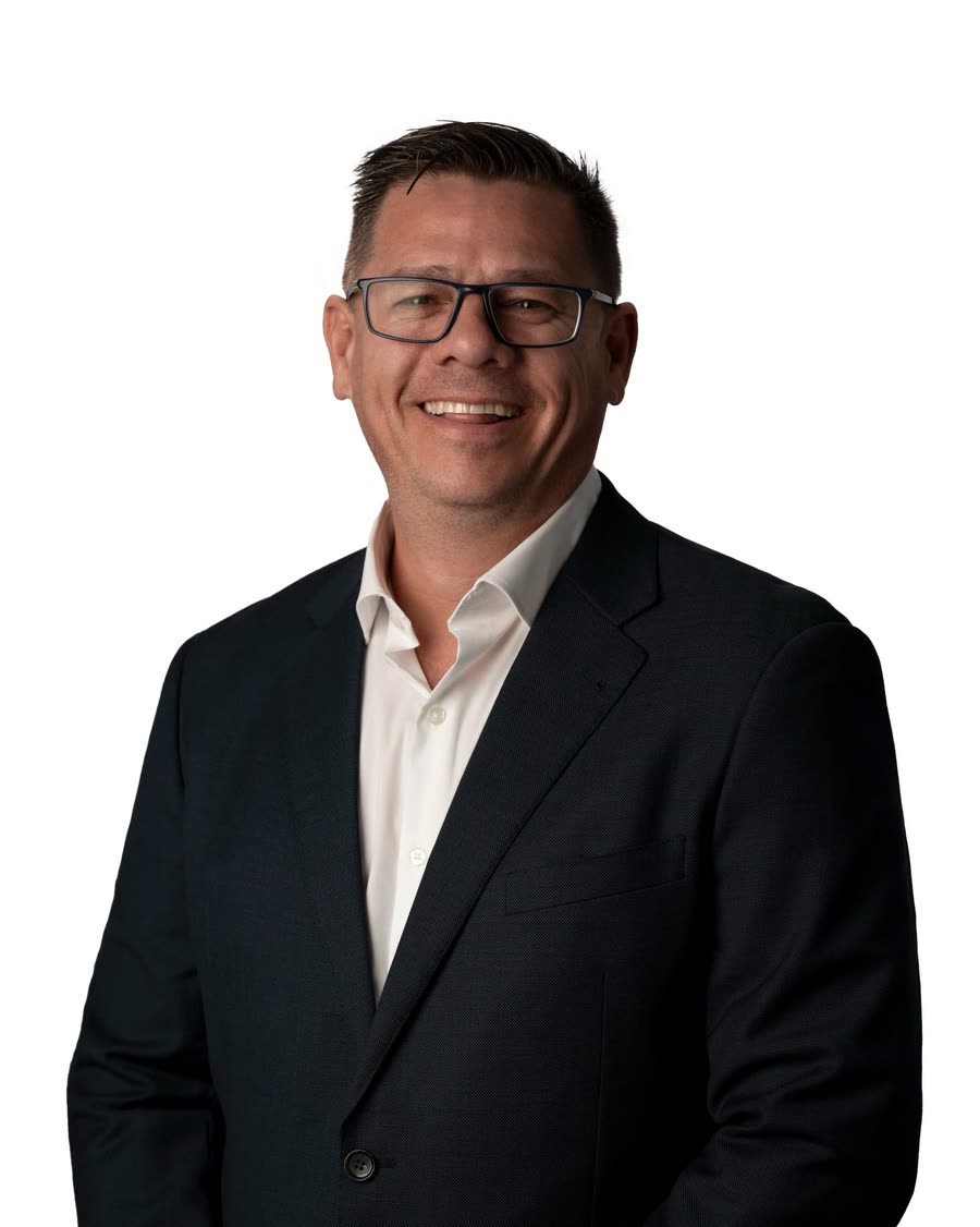 Studio headshot of a business leader in a black suit and glasses on white