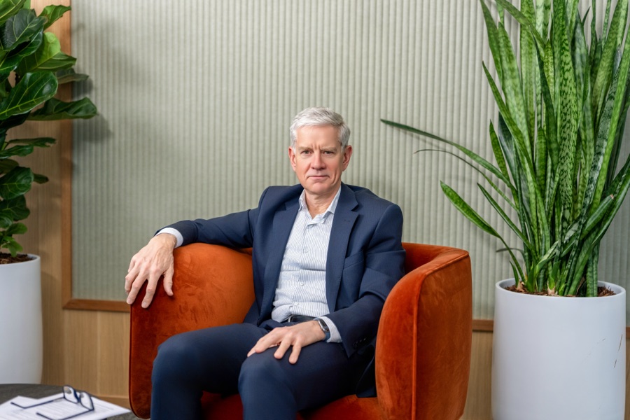 A seated portrait of a man in an orange armchair beside a plant