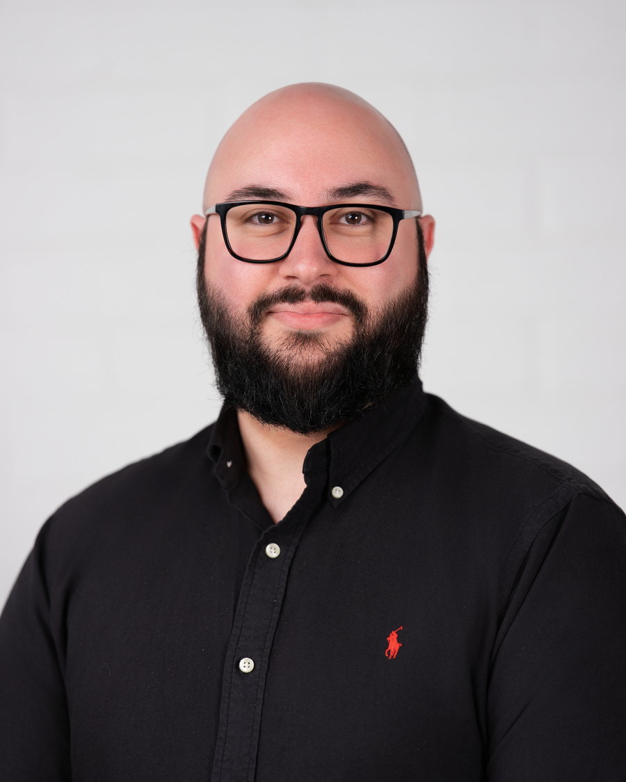 Studio headshot of a bearded team member in a black shirt and glasses on white