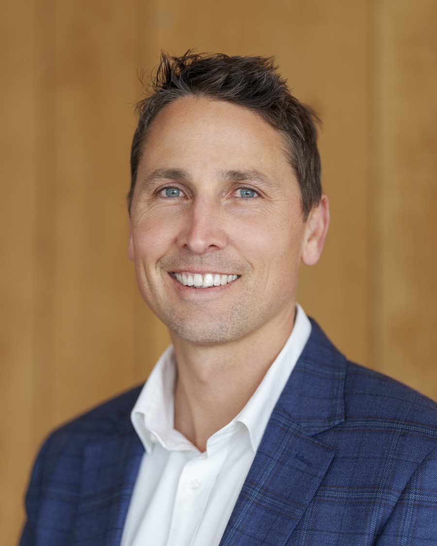 Corporate headshot of a professional in a blue check blazer against timber panelling