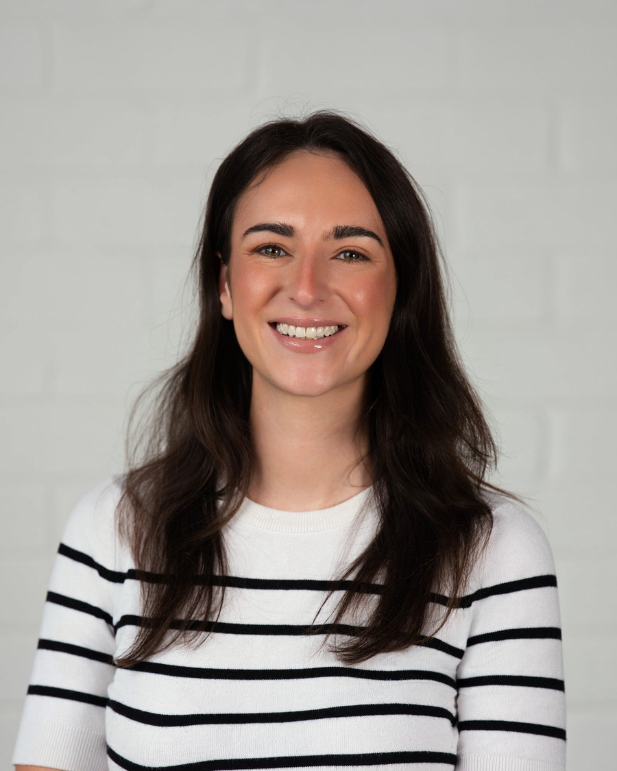 Headshot of a woman in a striped top against a white brick wall