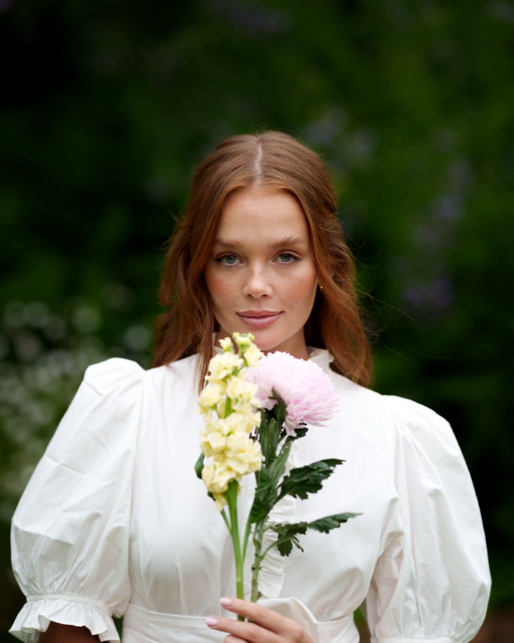Portrait of a woman in white holding cut flowers