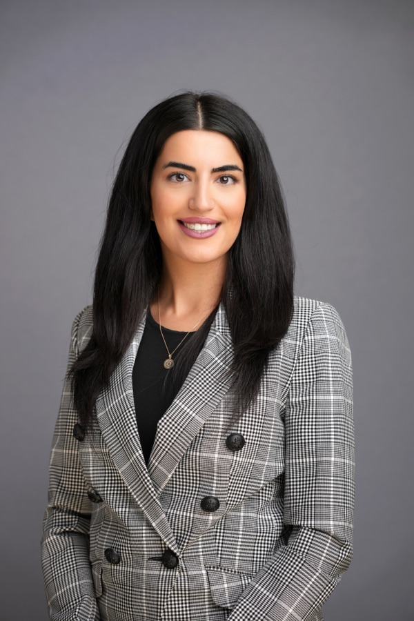 Corporate headshot of a woman in a checked blazer on a grey ground