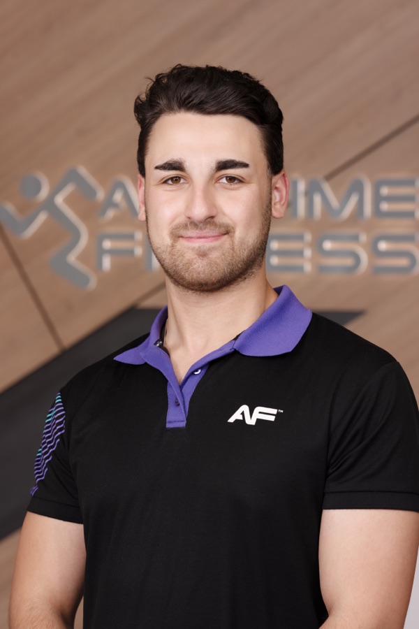 Studio headshot of a gym team member in a branded polo against a warm backdrop