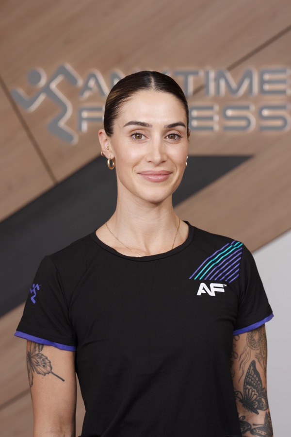 Studio headshot of a gym team member in a branded tee against a warm backdrop