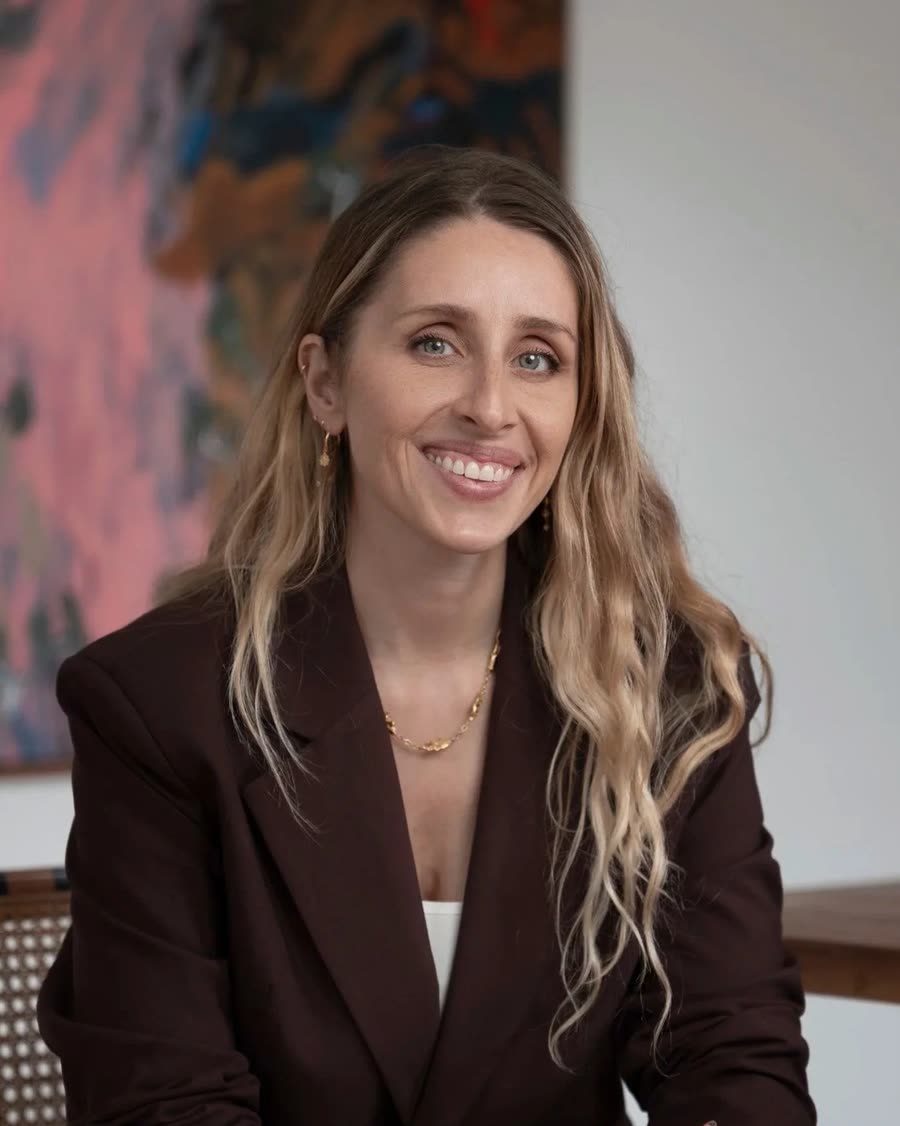 Corporate headshot of a professional in a burgundy blazer against artwork