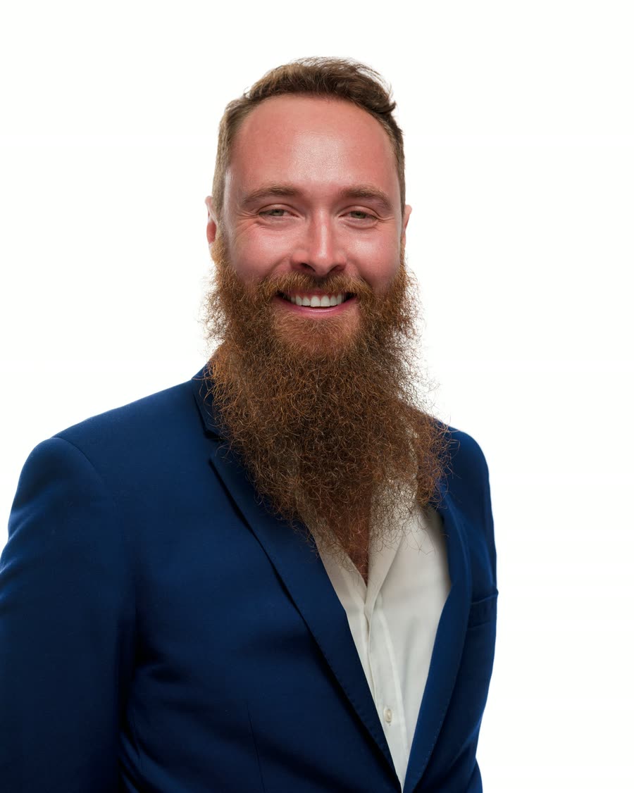 Studio headshot of a bearded professional in a navy blazer on a white background