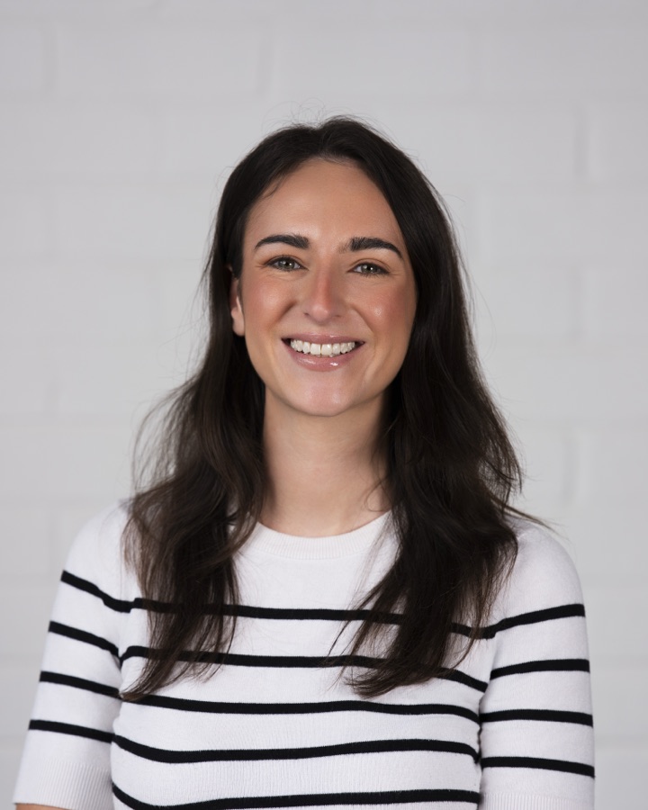 Headshot of a woman in a striped top against white brick