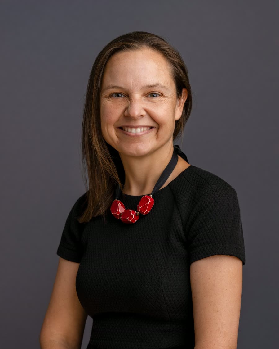 Corporate headshot of a professional in black with a red statement necklace on grey