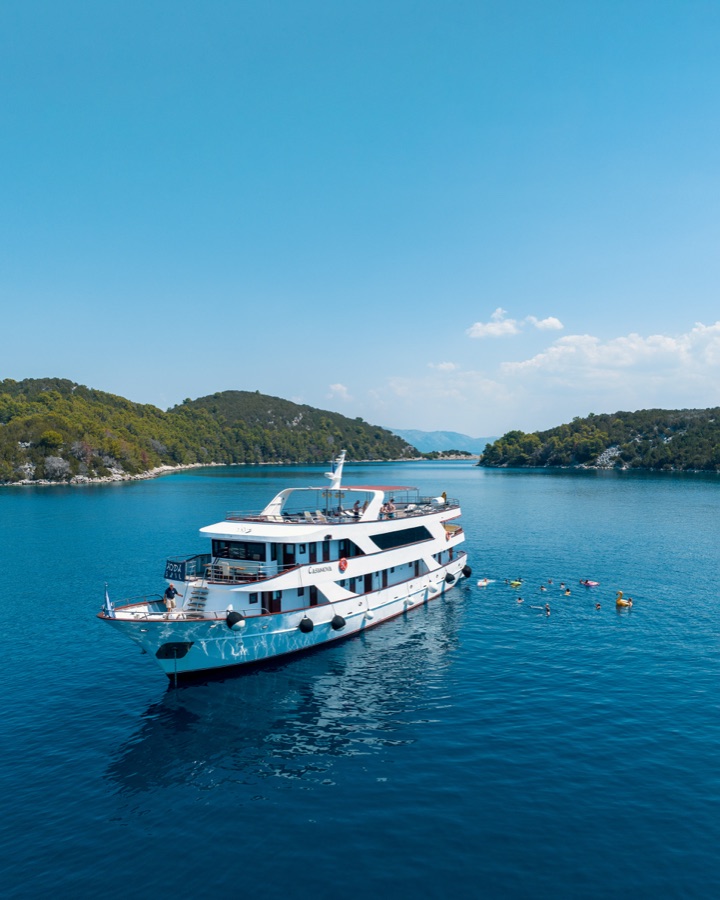 A motor yacht anchored in a blue bay below a headland