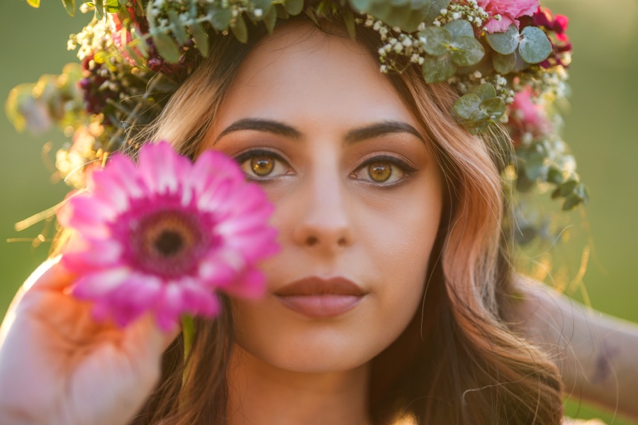A portrait in a flower crown holding a pink gerbera to the frame