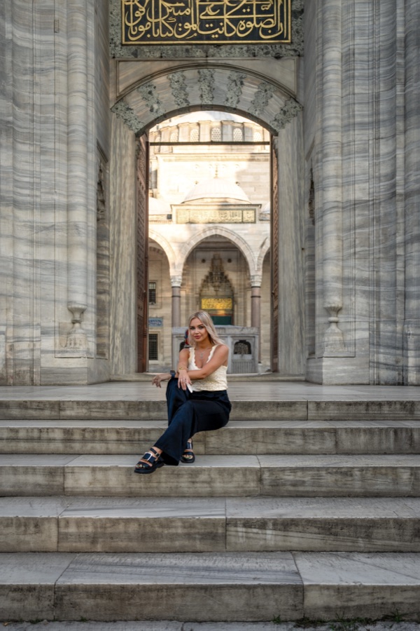 A woman seated on the steps of a stone mosque courtyard