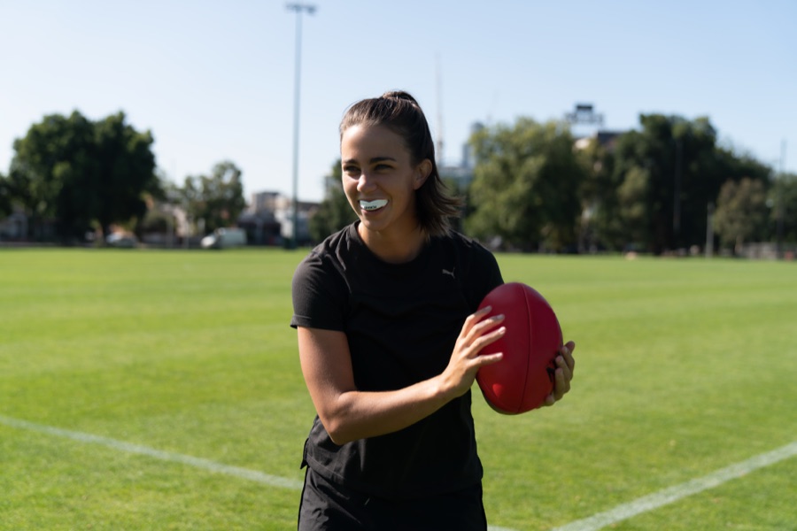 Footballer with a mouthguard holding a ball on a marked oval