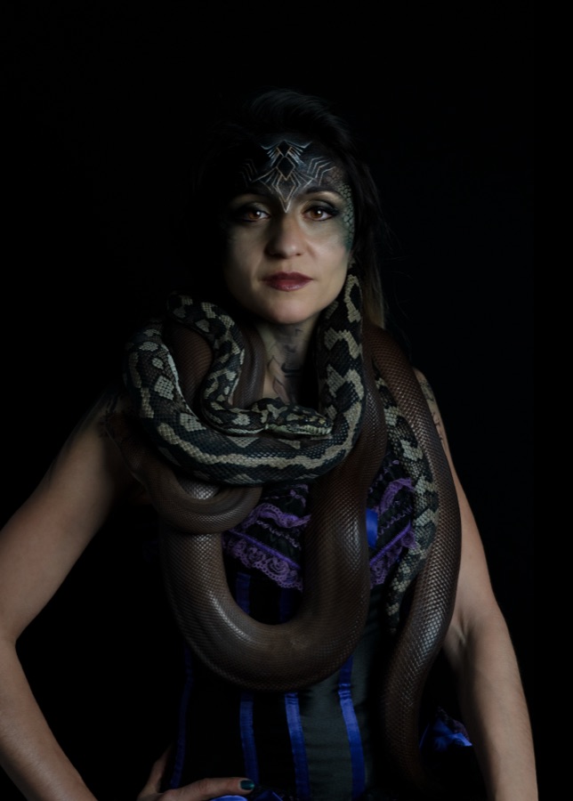 A studio portrait of a woman with a python across her shoulders