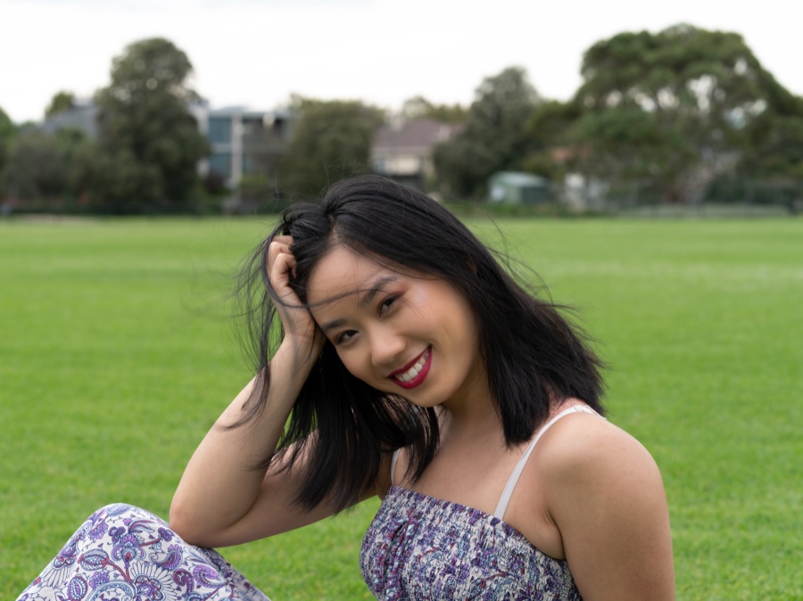 A woman seated on grass in a floral top, backlit by afternoon sun
