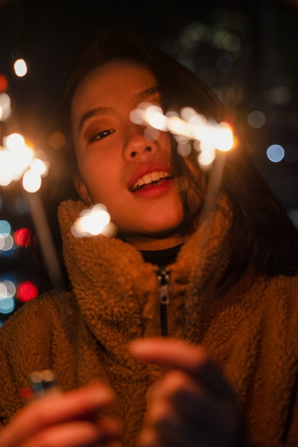 A woman holding a sparkler against city lights at night