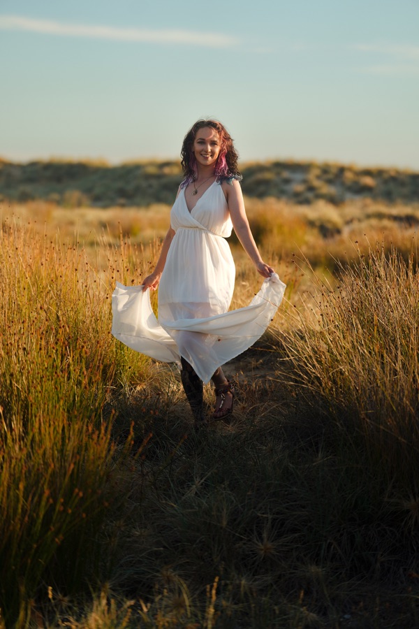 A woman in a white dress turning in golden coastal grass