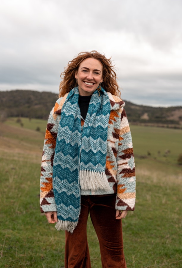 A woman in a patterned coat and scarf photographed in open country
